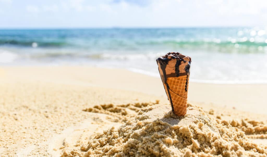 Ice cream cone on sand beach background / Melting ice cream on beach sea in summer hot weather ocean landscape nature outdoor vacation , ice cream chocolate