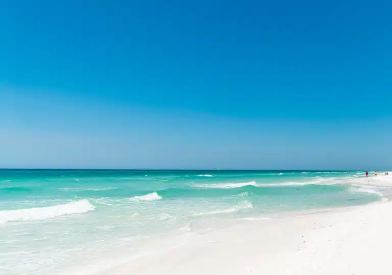 A weathered beach house sits on a white sand beach looking out o